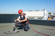 Ein Arbeiter in voller PSA fotografiert einen installierten Anschlagpunkt auf einem Flachdach zur Dokumentation.